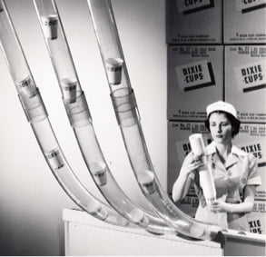 An employee in a cup production company loading cups into pneumatic tubing in the 1950s