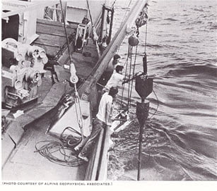Black and white photo of an oceanographic research ship pulling a core sample tubing rig from the ocean floor.