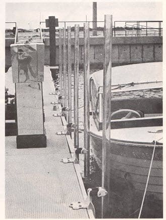 An old black and white photo of heavy tubing lining a Florida Marina where a small boat is docked.