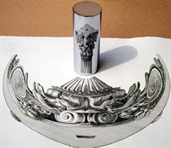 A distorted image of a Corinthian pillar capital next to a mirror cylinder showing the proper image in a reflection