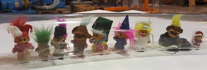 Nine troll dolls lined up inside of a clear tube