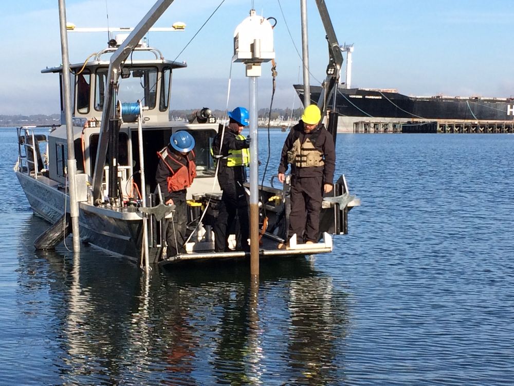 A marine core sample tubing being pulled out of the water in a harbor