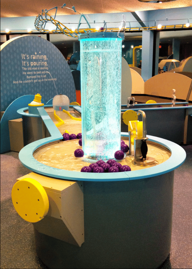 An illuminated tube filled with sparkling liquid in a children's museum display.